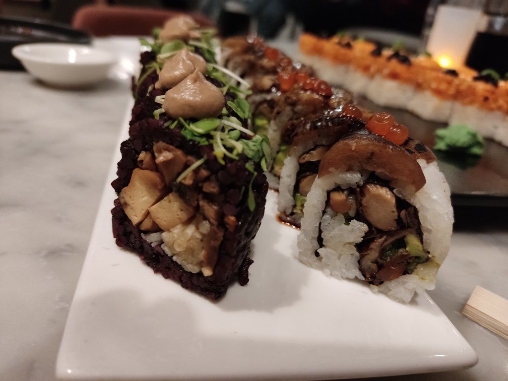 On the left, sushi rolls with black rice and a mushroom filling. On the right, sushi rolls with white rice and mushroom, avocado, and aubergine filling