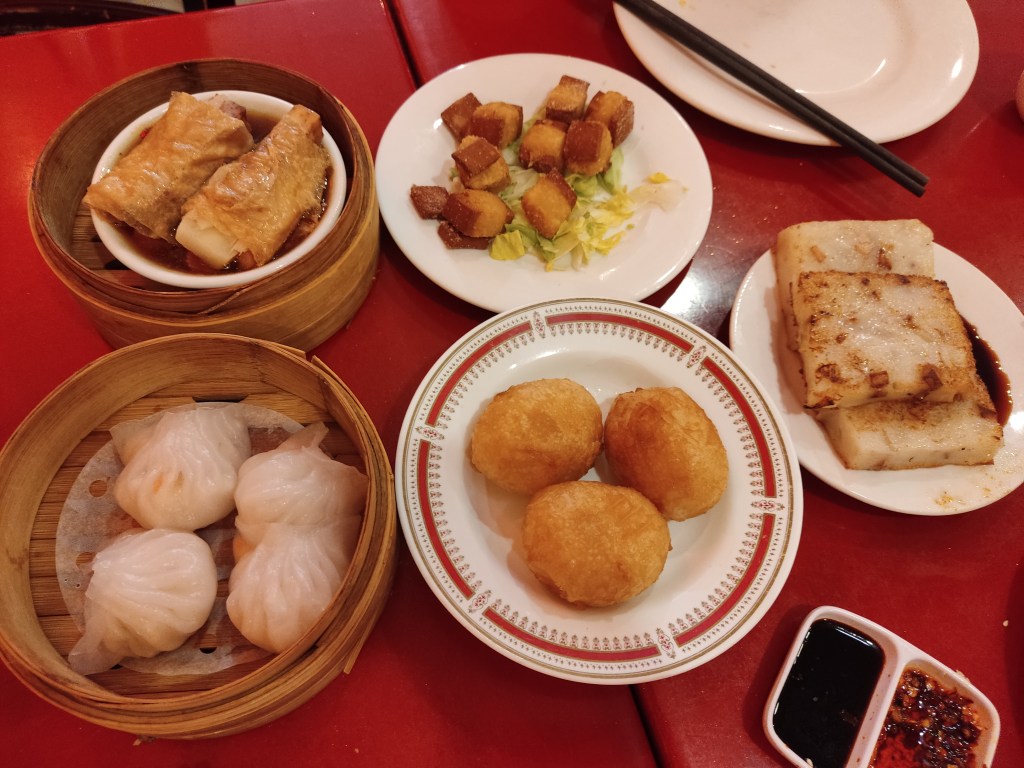 An array of dim sum dishes serves on plates and steamers with sauces on the side