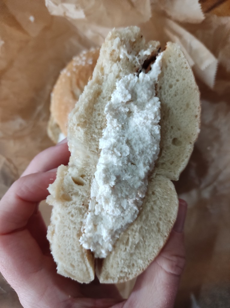 A bagel sliced in half with the cut side facing the camera, showing a thick layer of tofu cream cheese