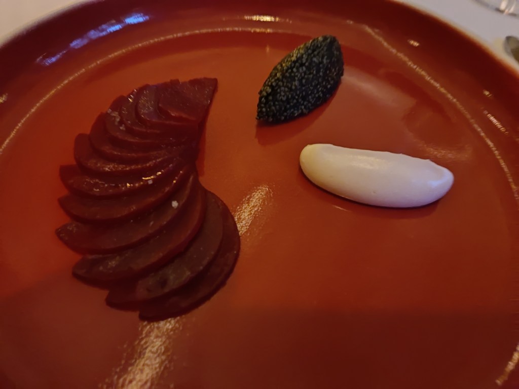 A red plate with artfully arranged beetroot slices and quenelles of a seaweed black cream and a white horseradish cream