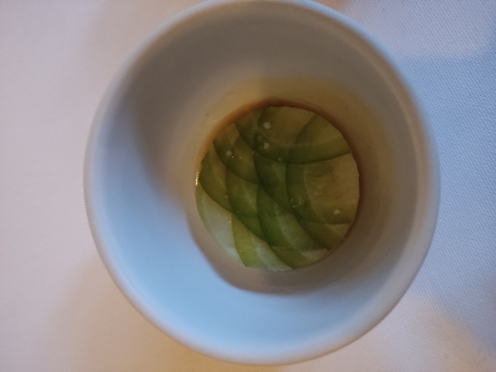 A small dish containing a small dumpling topped with overlapping circles of green radish