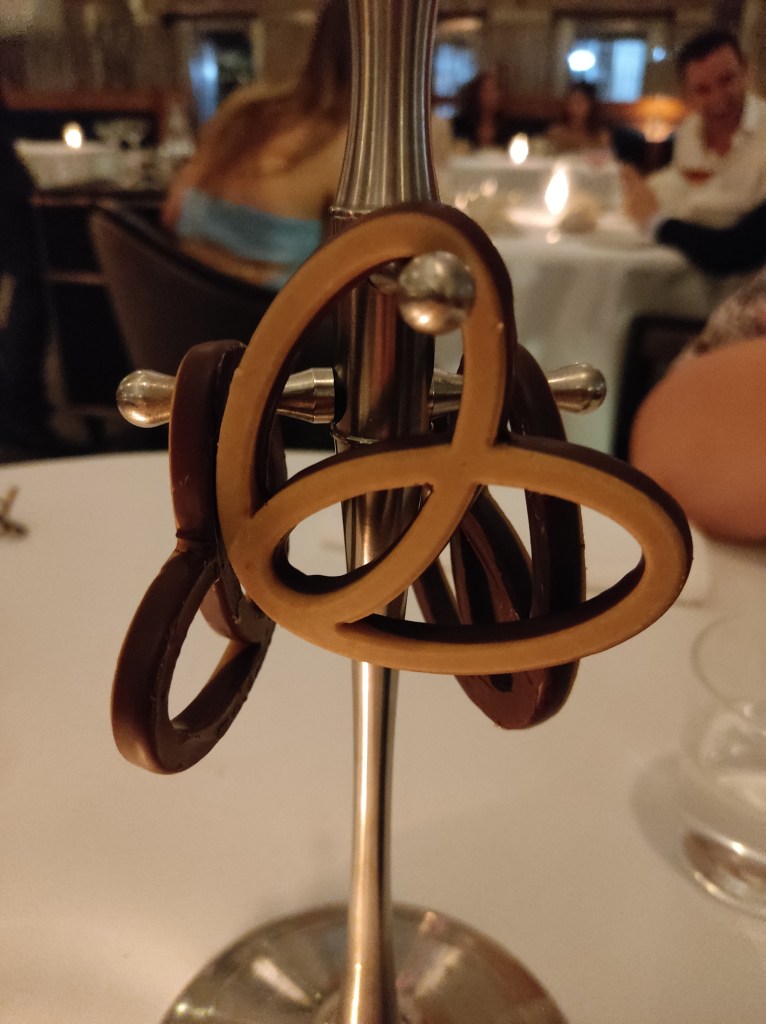 Three delicate chocolate covered pretzels hanging from a stand