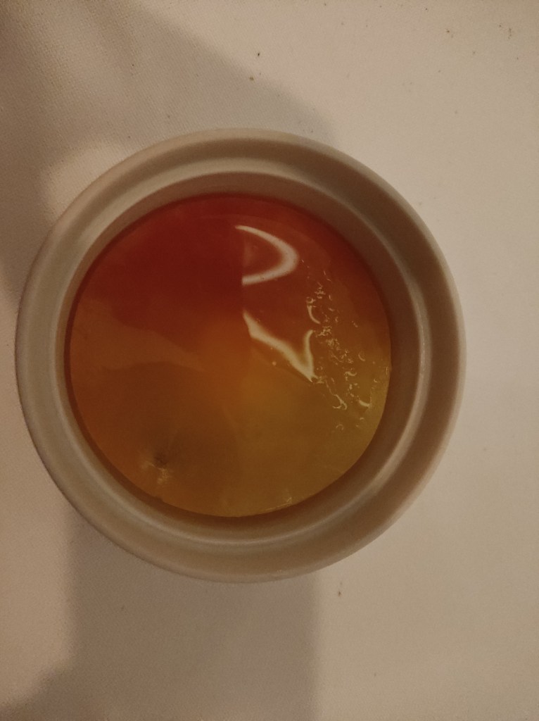 A small dessert dish with a glossy orange disc covering the dessert below