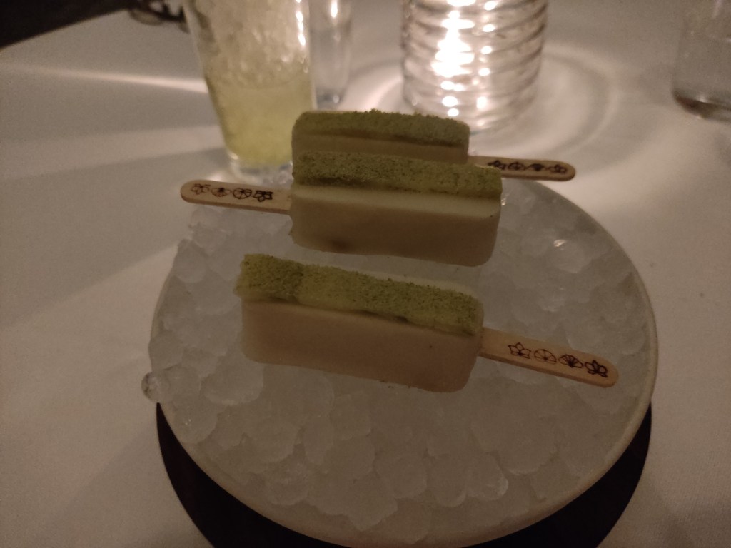 Three white popsicles with a green stripe on top, sitting on a bowl of ice