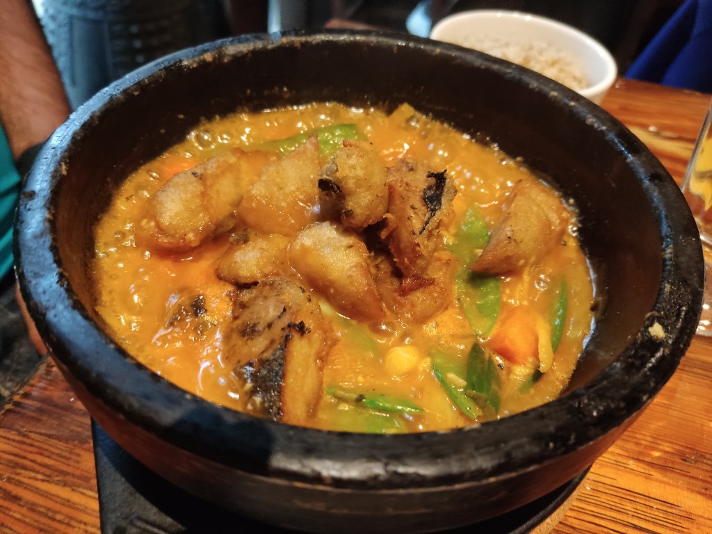 A hot pot filled with a thick golden stew containing vegetables and fishy chunks including some deep fried chunks