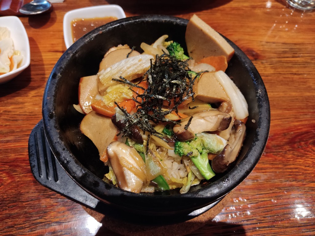 A very hot stone bowl filled with vegetables, rice, tofu, and seaweed