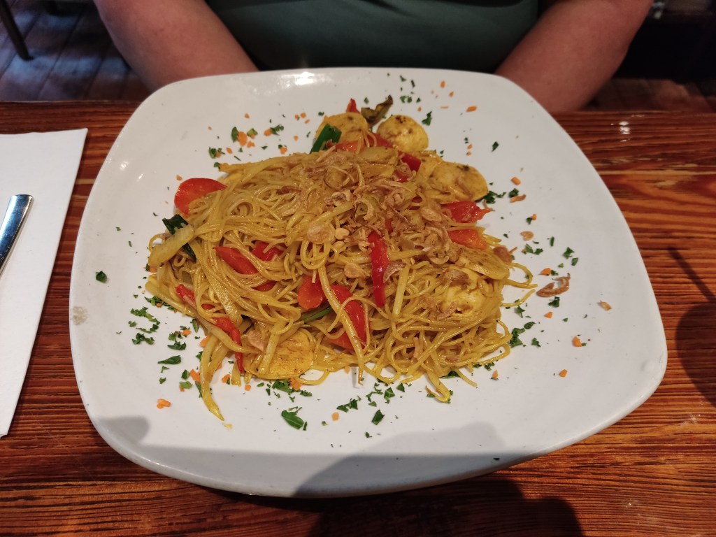 A large plate of noodles with red peppers, herbs, and some fishy chunks