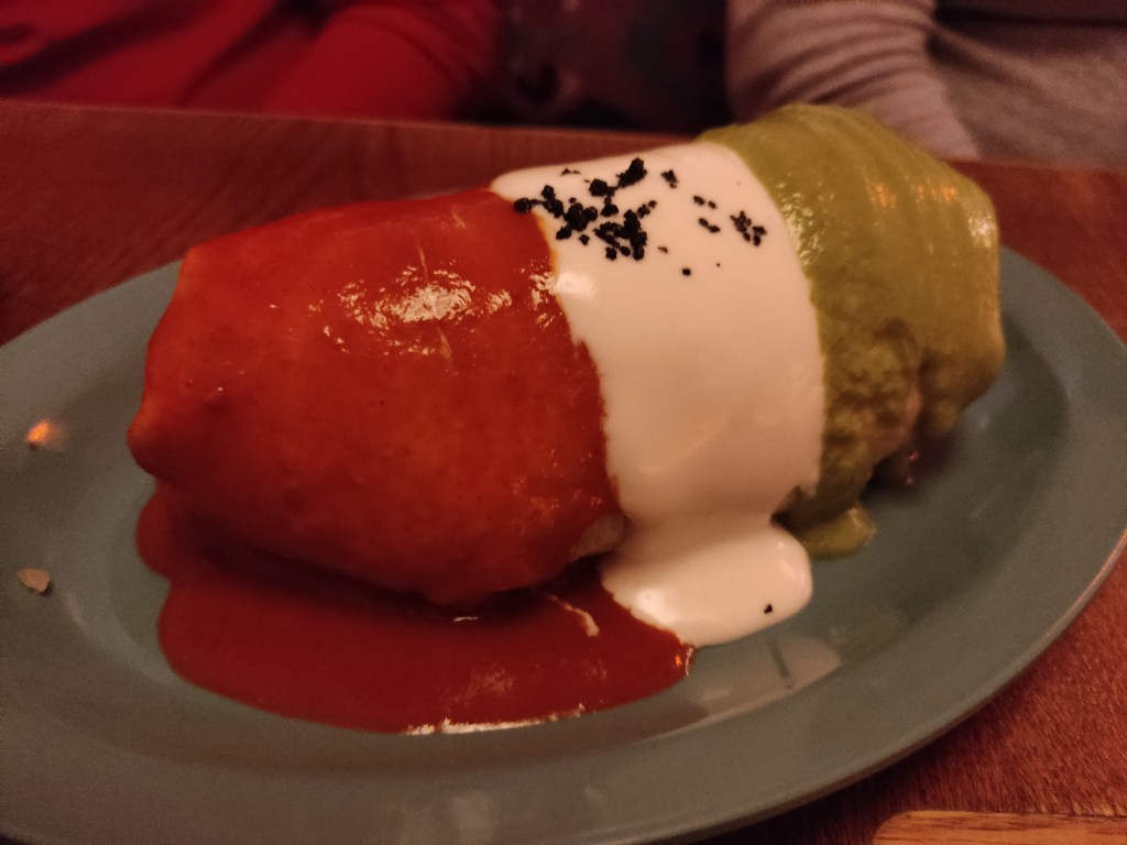 A large burrito smothered in stripes of red, white, and green sauces
