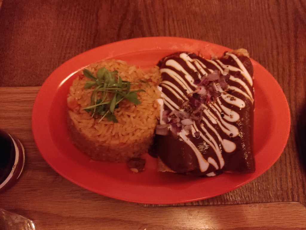 Enchiladas covered in mole sauce and drizzled with sour cream with rice on the side