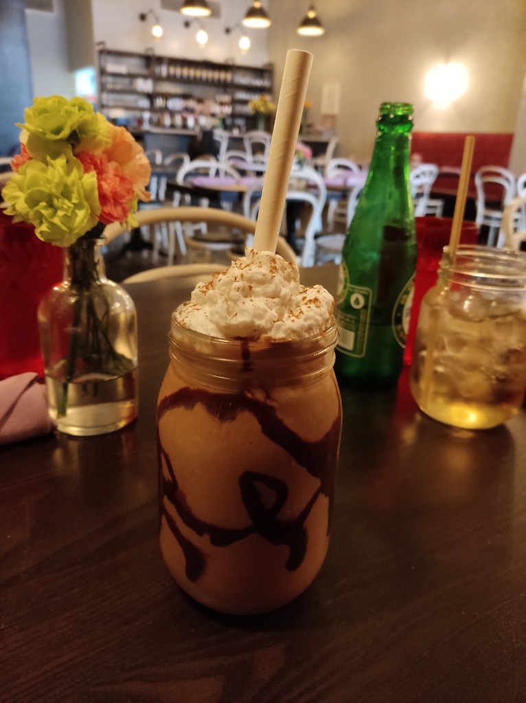 A glass filled with chocolate milkshake with chocolate sauce swirled around the inside of the glass and cream on top
