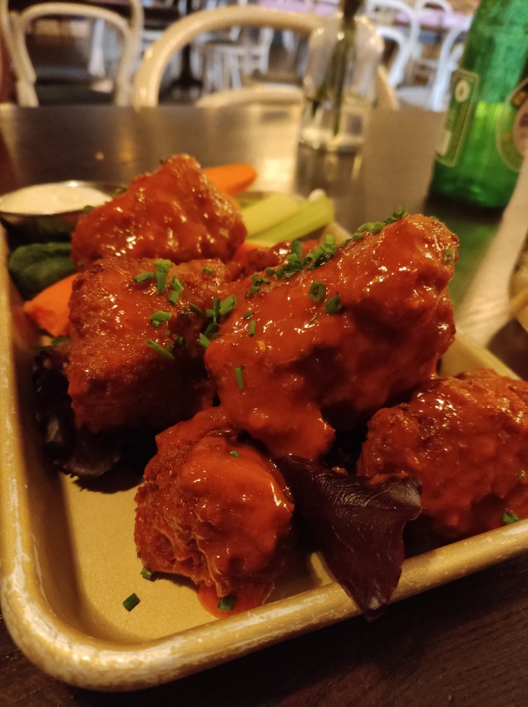 Seitan wings covered in buffalo sauce, with some vegetables and ranch dressing in the backgorund
