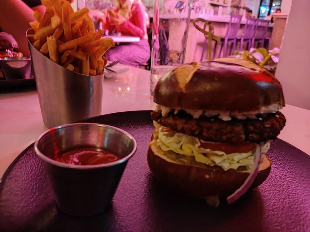 A burger in a pretzel bun with salad, a patty, and blue cheese. Fries on the side.