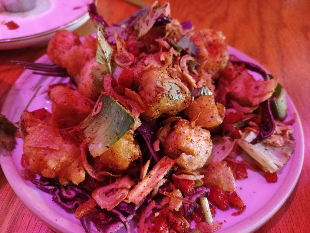 A plate piled high with deep fried salt and pepper tofu, with some vegetables.