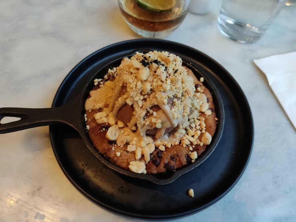A cookie skillet topped with a huge portion of chocolate ice cream and drizzled with peanut butter