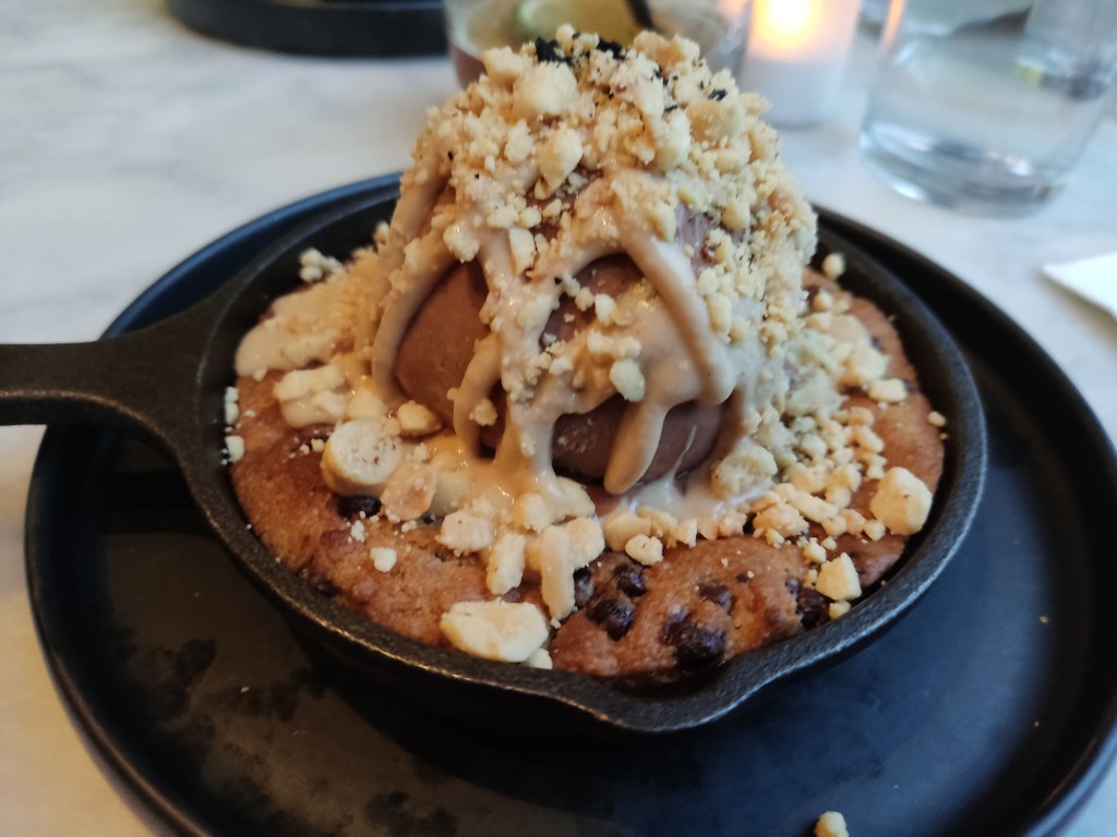 A cookie skillet topped with a huge portion of chocolate ice cream and drizzled with peanut butter