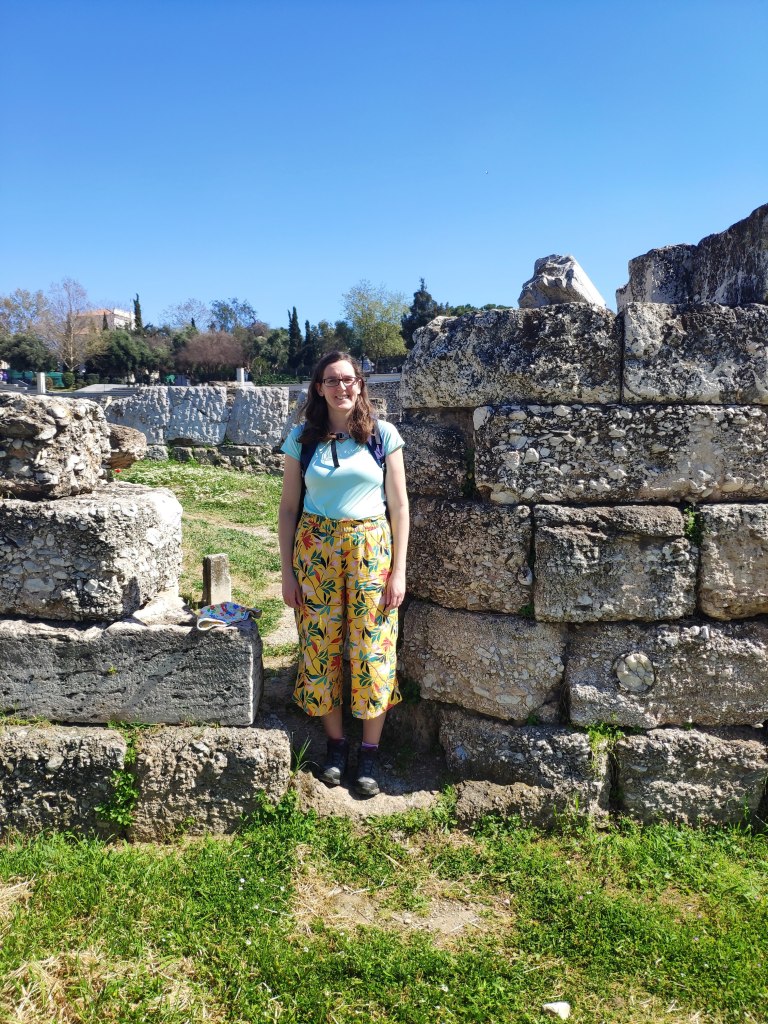 Jenny is standing at the archaeological site of Keramikos amongst some ruins