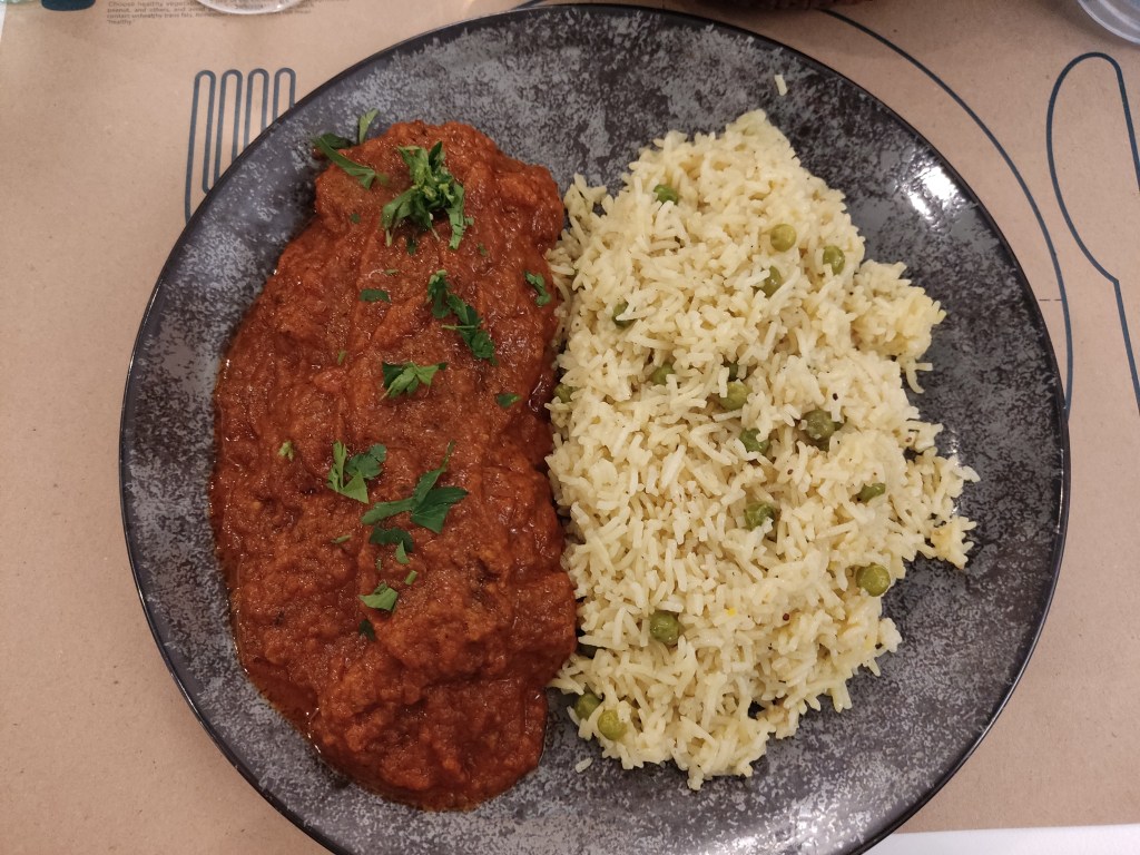 A large serving of a tomatoey sauce and rice with peas, topped with herbs