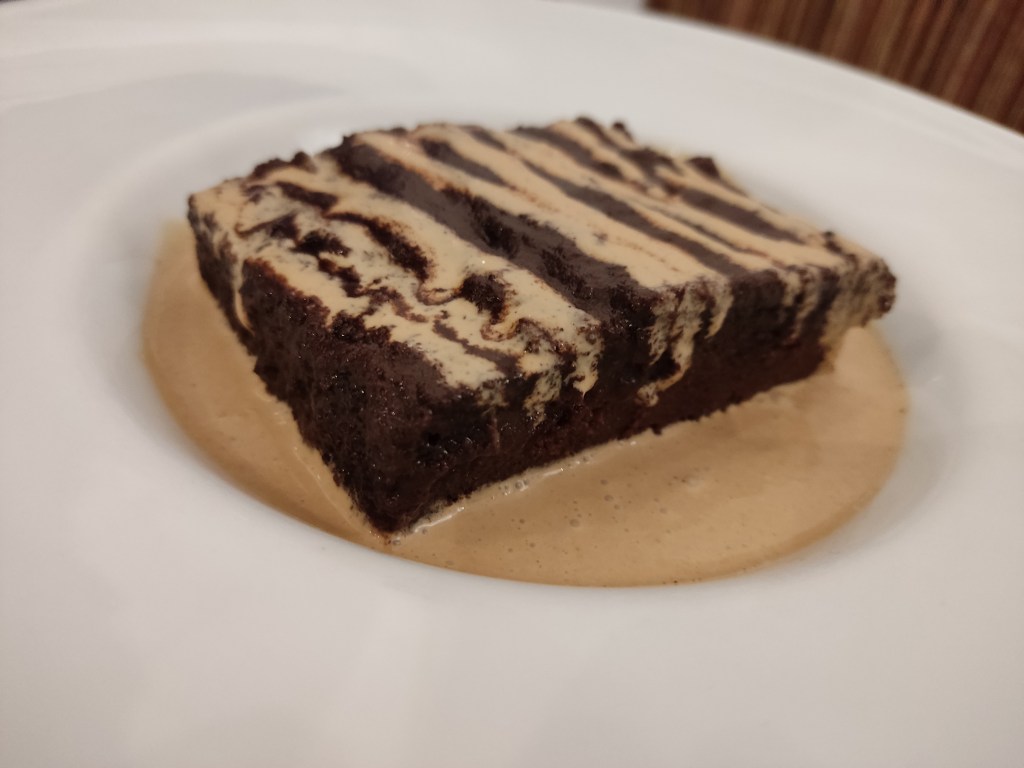 A large chocolate brownie in a pool of creamy sauce