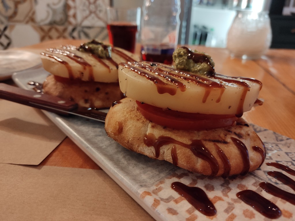 Fried bread topped with a slice of tomato and a thick slice of halloumi, drizzled with balsamic vinegar
