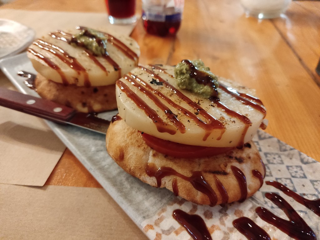 Fried bread topped with a slice of tomato and a thick slice of halloumi, drizzled with balsamic vinegar