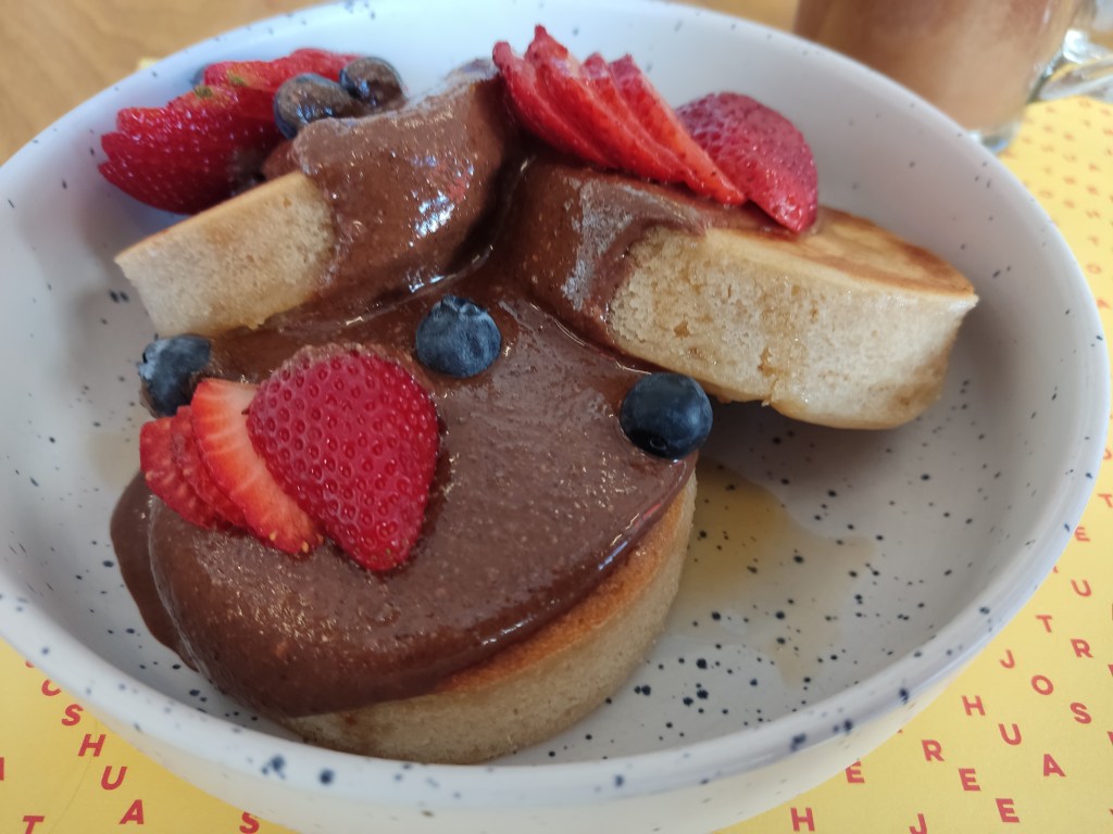 Three thick, fluffy hot cakes topped with chocolate sauce and fresh strawberries and blueberries