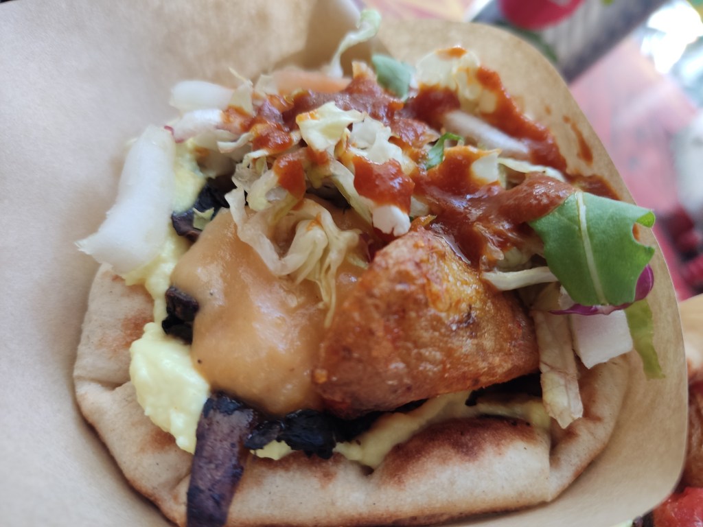 A fluffy pita filled with mushrooms, salad, and potato drizzled with barbecue sauce