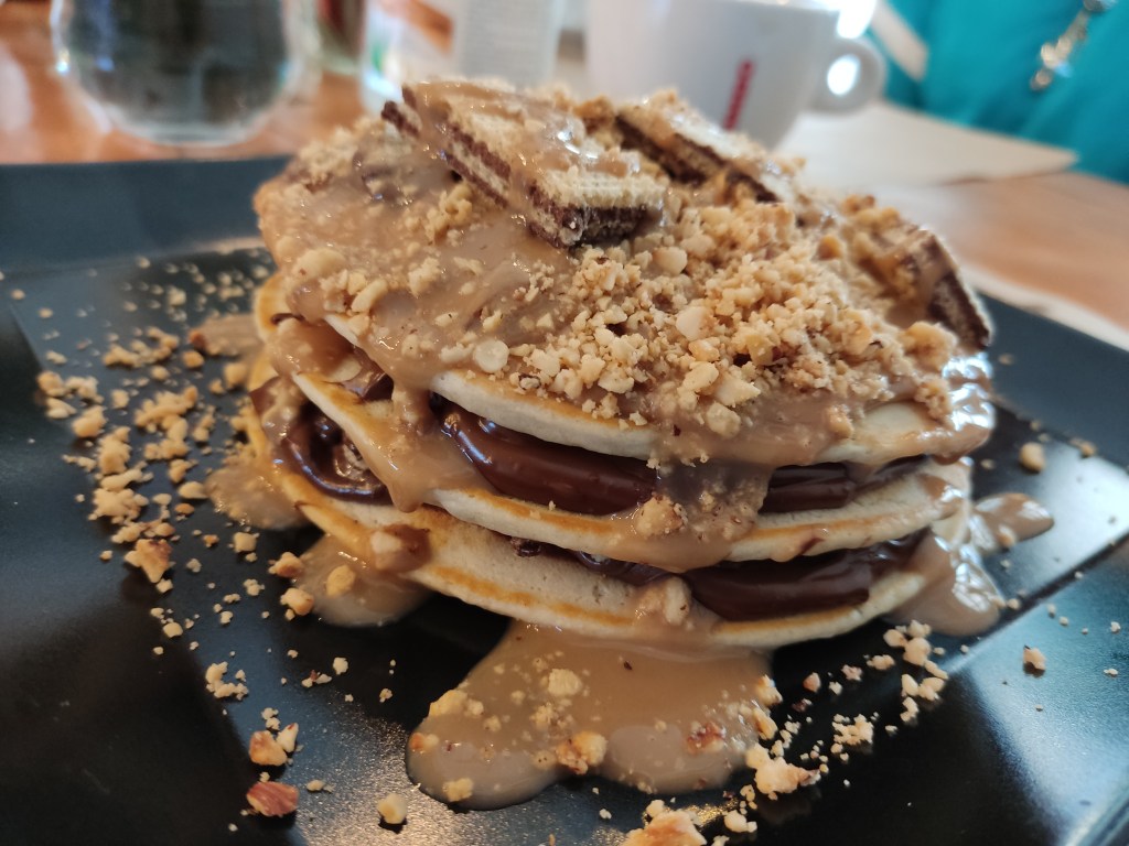 Three pancakes sandwiched with chocolate cream and covered in sauces, wafers, and crumbs