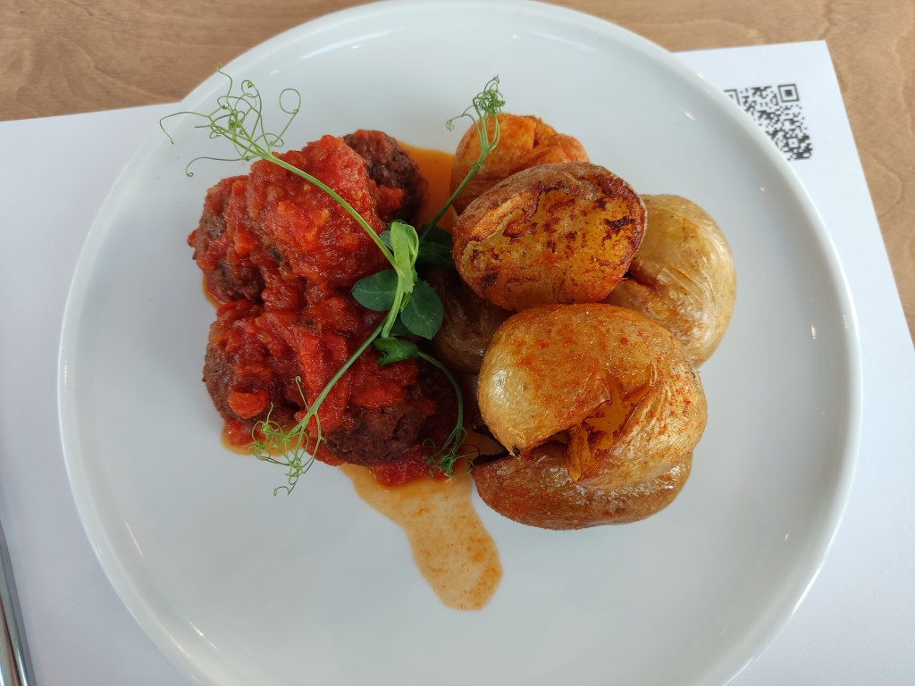 Meatballs under a tomato sauce with roasted potatoes on the side