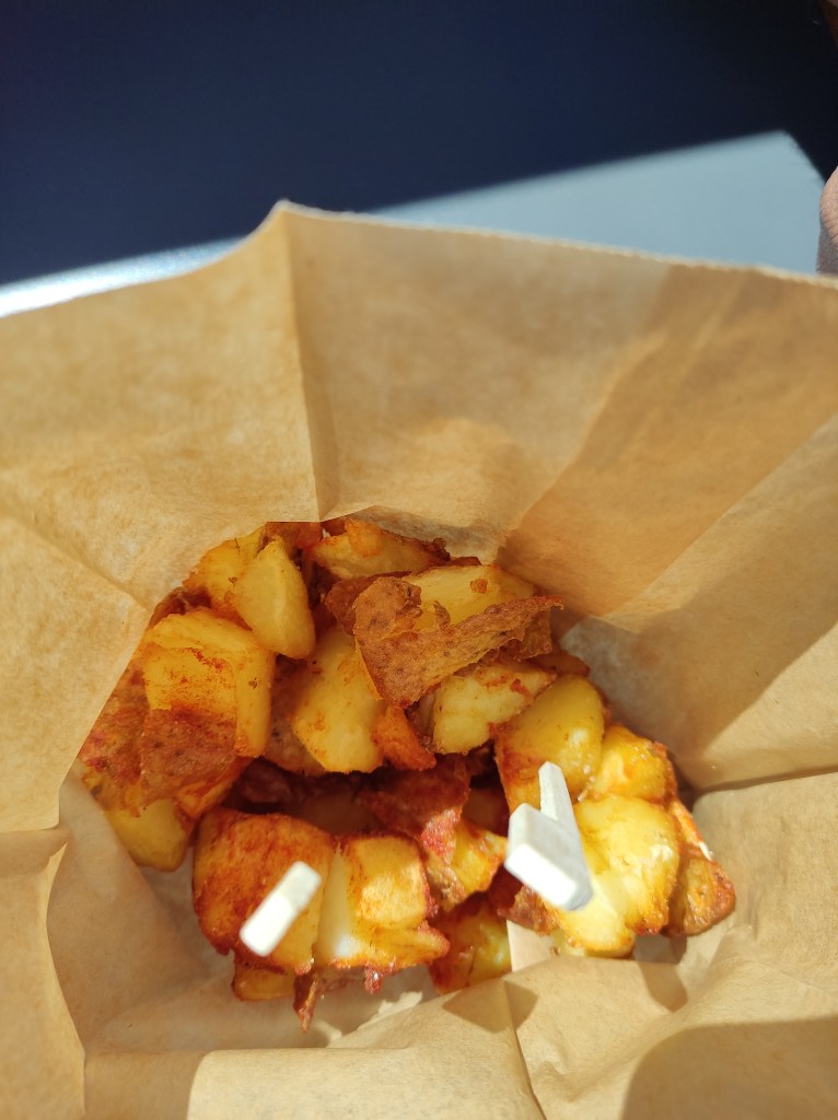 A paper cone filled with small crispy chunks of roasted potato