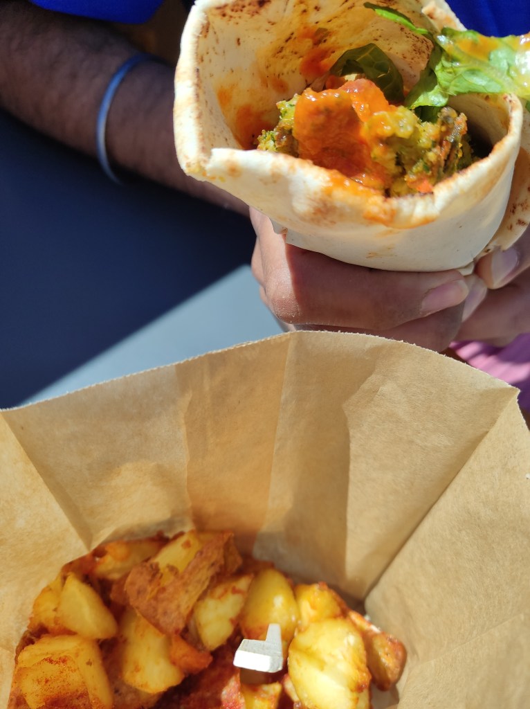 A falafel wrap drizzled with red sauce and a cone of potato chunks