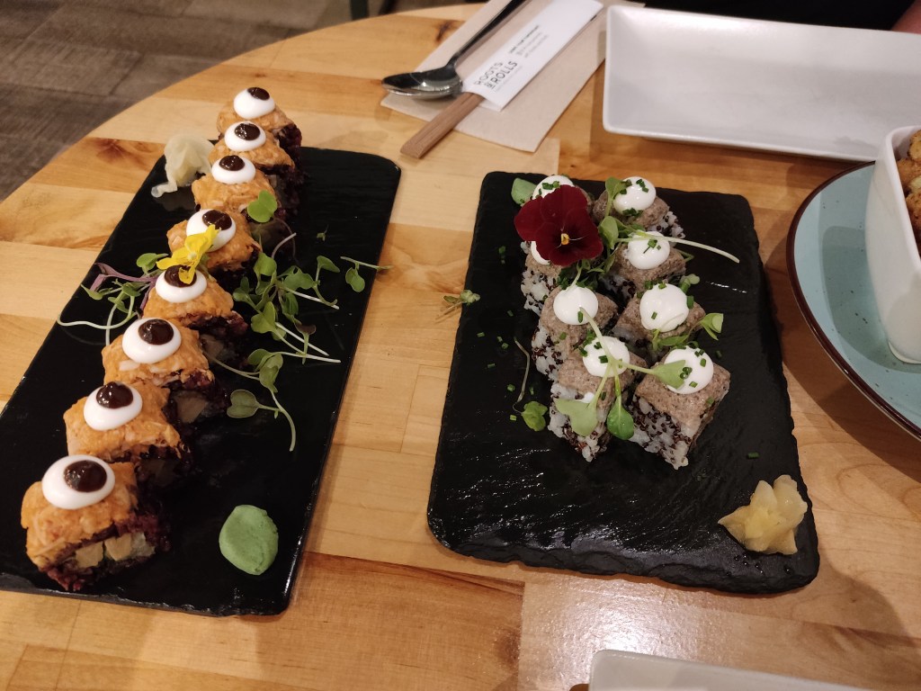 Two black slates each containing eight portions of sushi. 