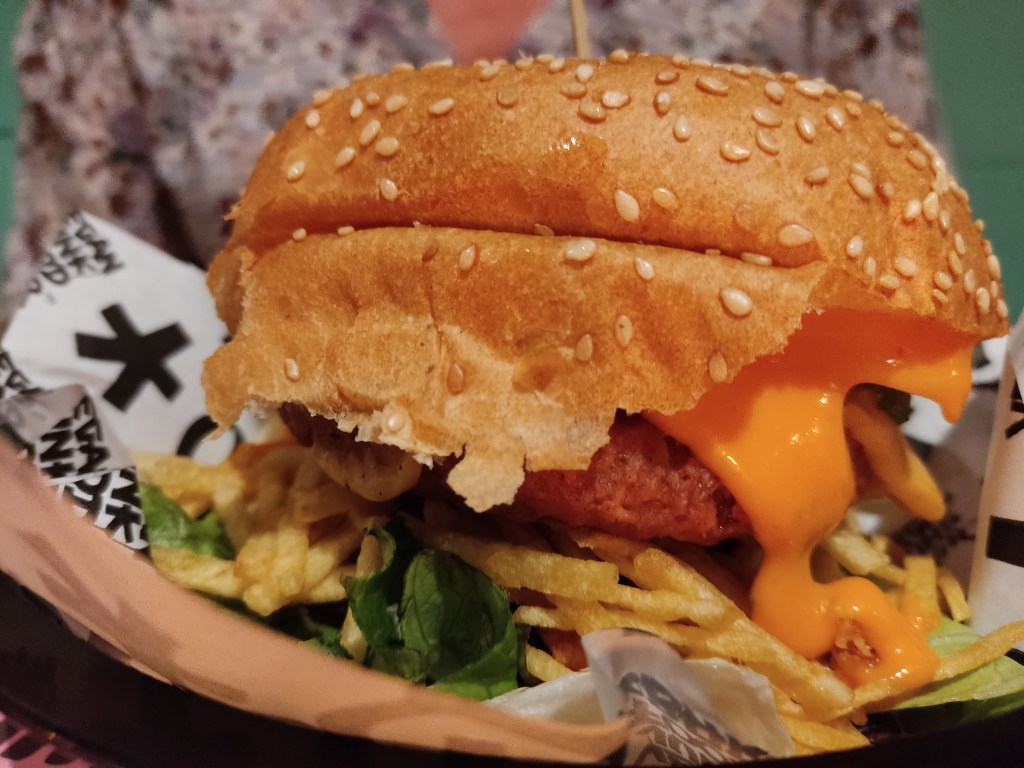 A big burger in a regular bun with cheese oozing down the side and lots of chipsticks 