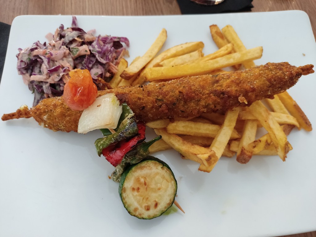 Deep fried chicken on a skewer with fries, a small skewer of roasted veg, and some coleslaw