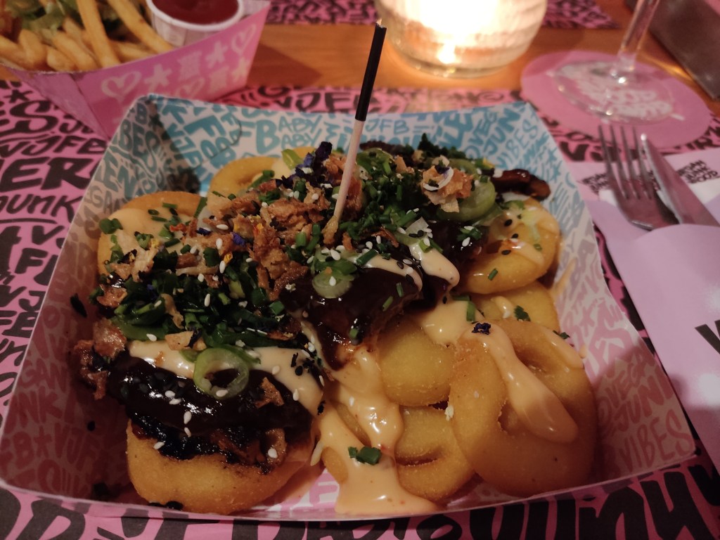 A tray filled with potato smiley faces topped with sticky ribs and sauce, fried onions, and spring onions