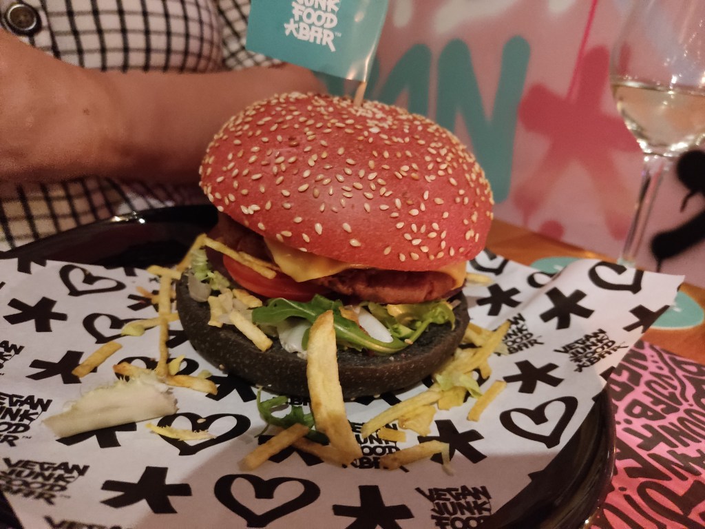 A big burger with a black bun on the bottom and a pink pun on top