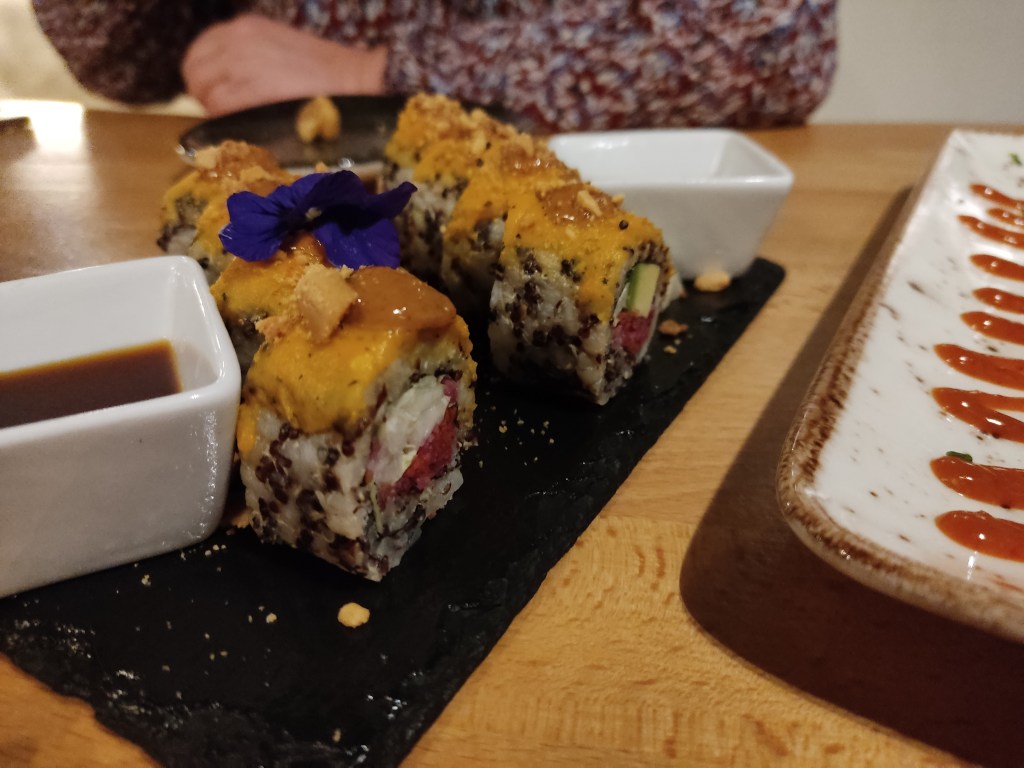 A slate with eight portions of sushi, rice on the outside, dark red filling in the middle, and orange sauce on top