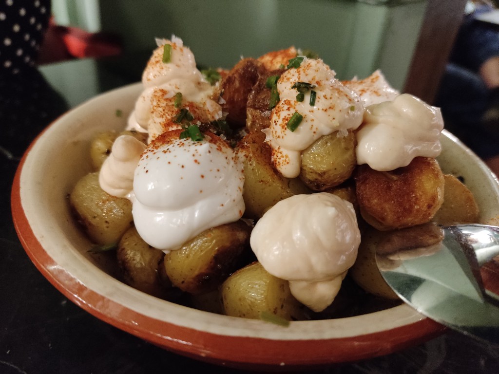 A bowl piled with small, well cooked potatoes and blobs of white cream dusted with spice and chives