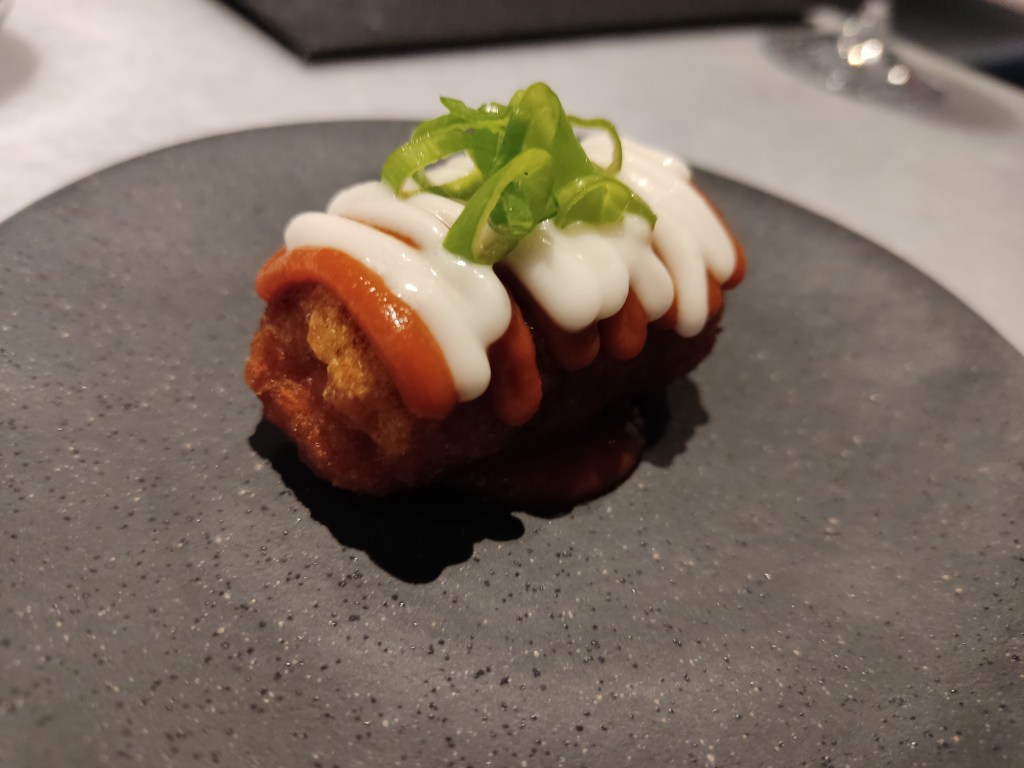 A deep fried potato croquette topped with piped white and red sauces and a spring onion garnish