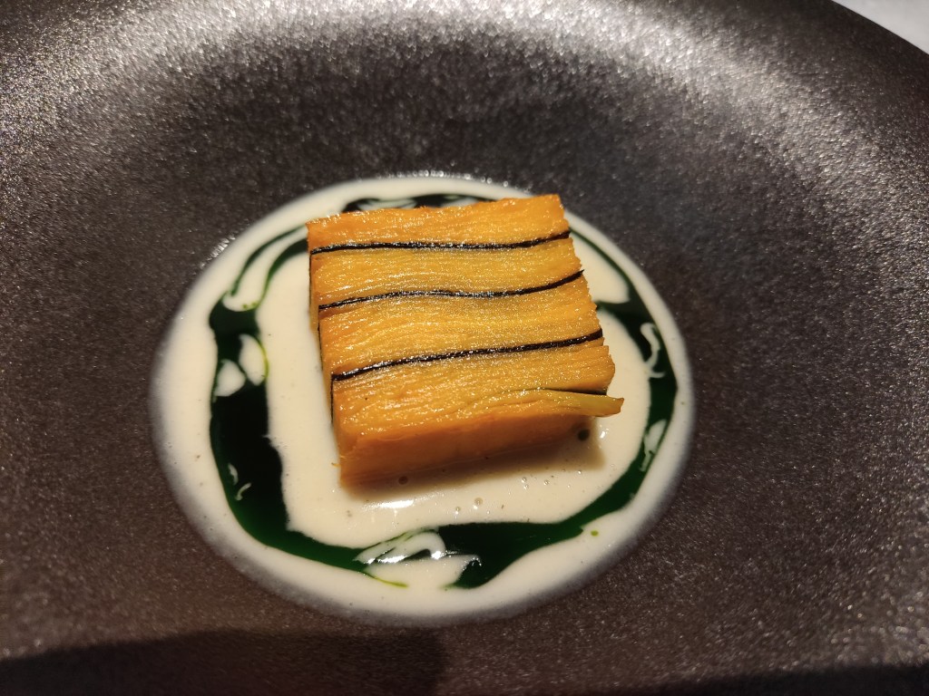 Thin layers of sweet potato in a terrine with a few nori layers in between, sitting in a creamy sauce split with green oil