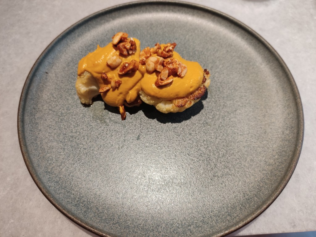 Two large florets of cauliflower tinged brown, topped with a yellow sauce and chunky peanuts