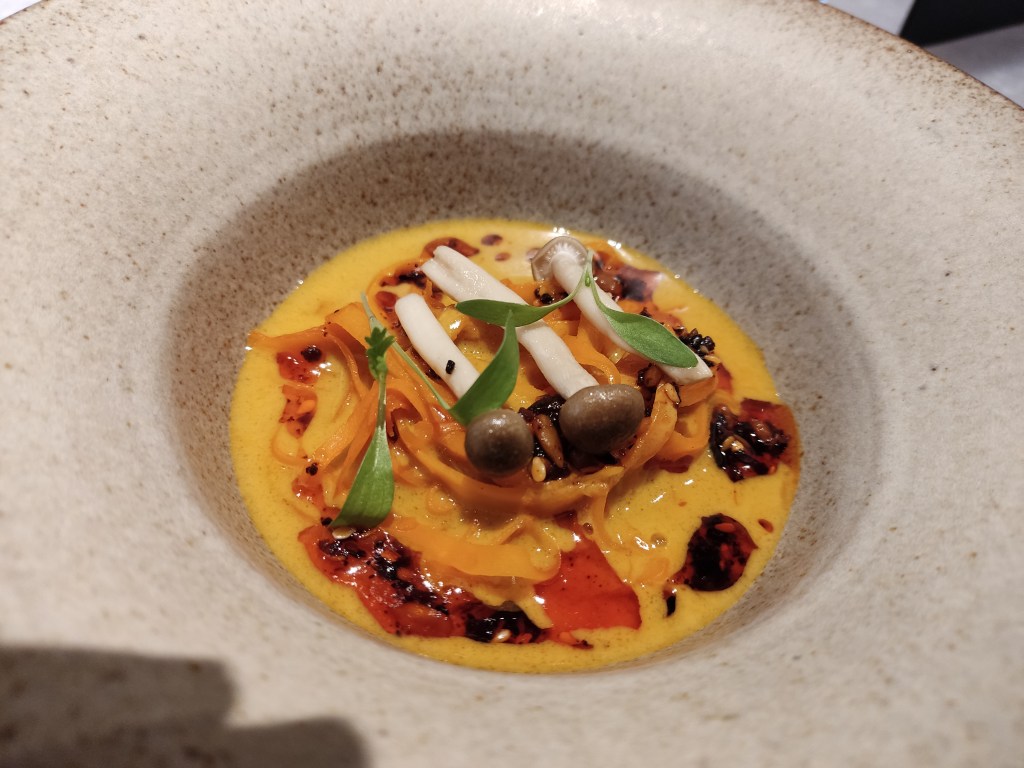 A bright yellow broth filled with noodles, mushrooms, and herbs, split with red oil