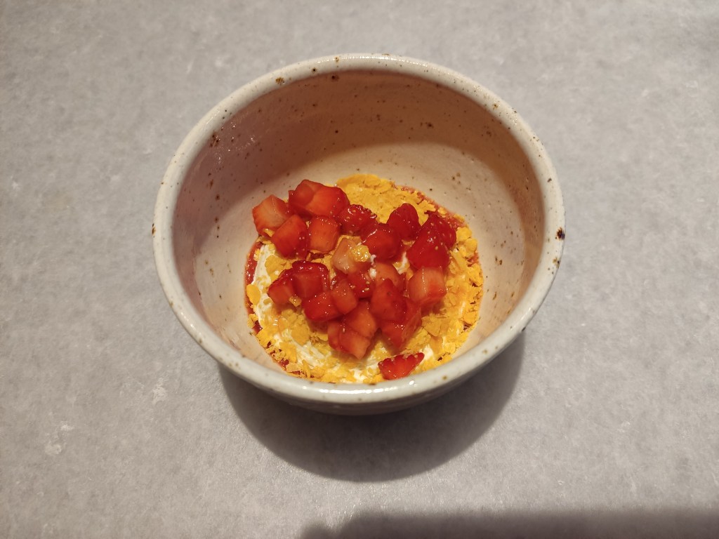 Diced strawberries covering crushed flakes on top of a small scoop of cream