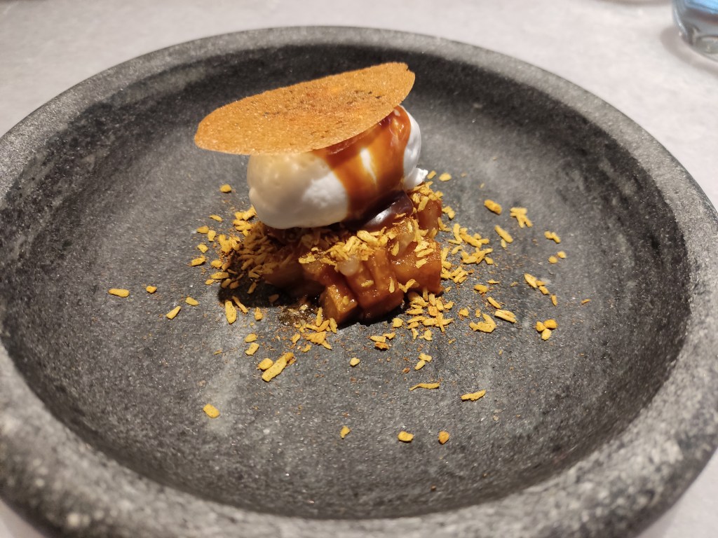 Pineapple chunks underneath a scoop of white ice cream drizzled with a caramel coloured sauce, with a thin delicate tuille on top.