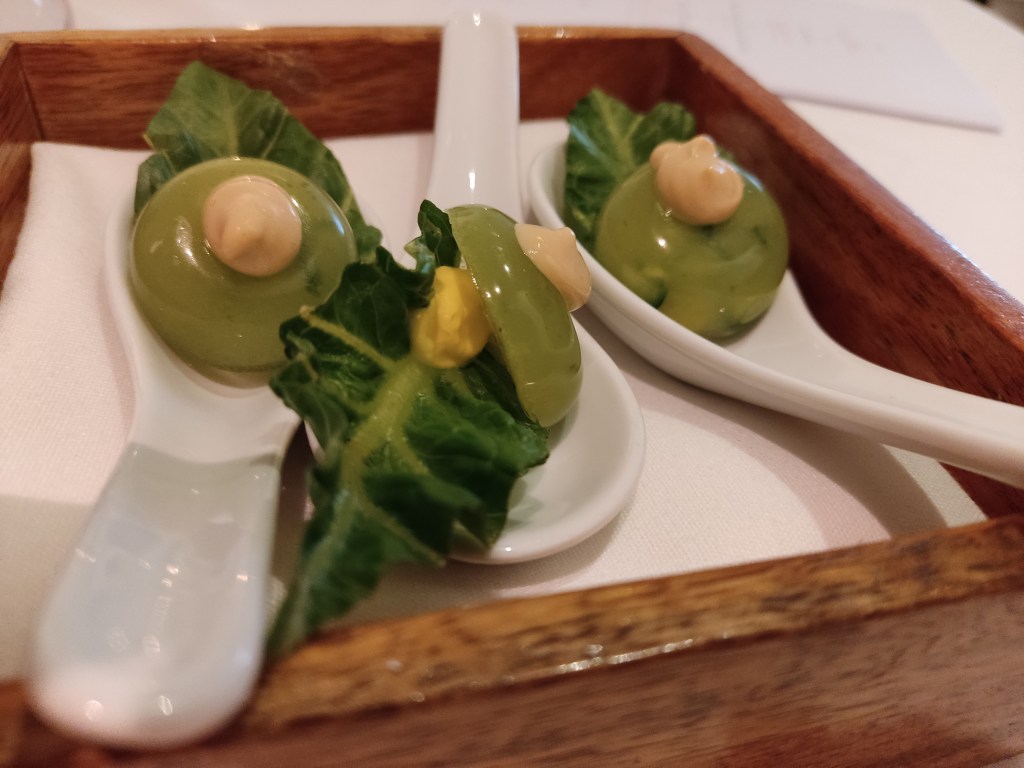 Three spoons each holding a green leaf and a green jelly topped with a beige cream