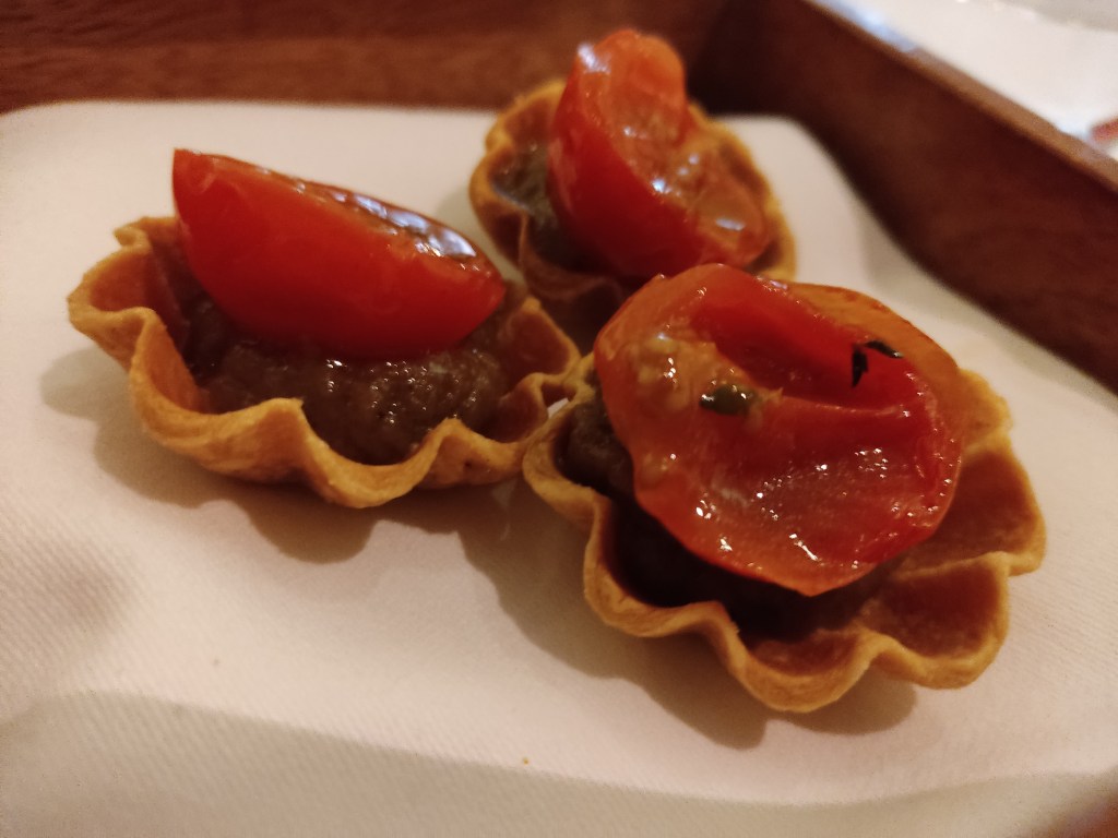 Three small tarts with thin cases, a brownish gel and a cherry tomato half