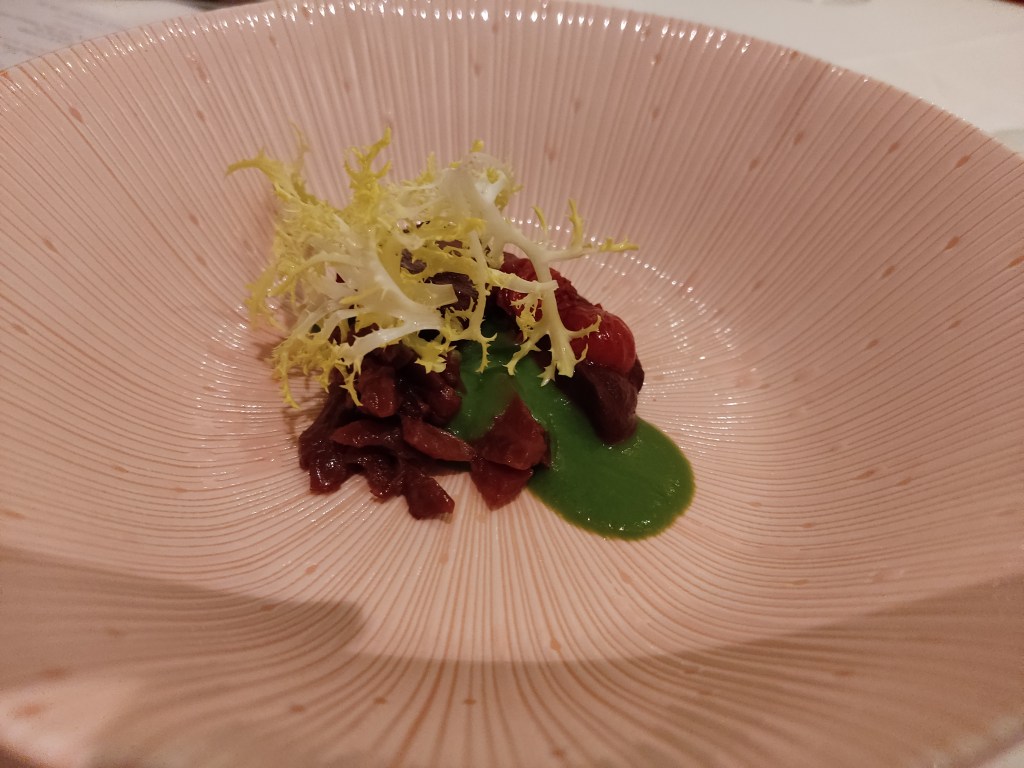 Chopped beetroot next to a small pool of green sauce, alongside a smooth helping of puree and topped with some leaves