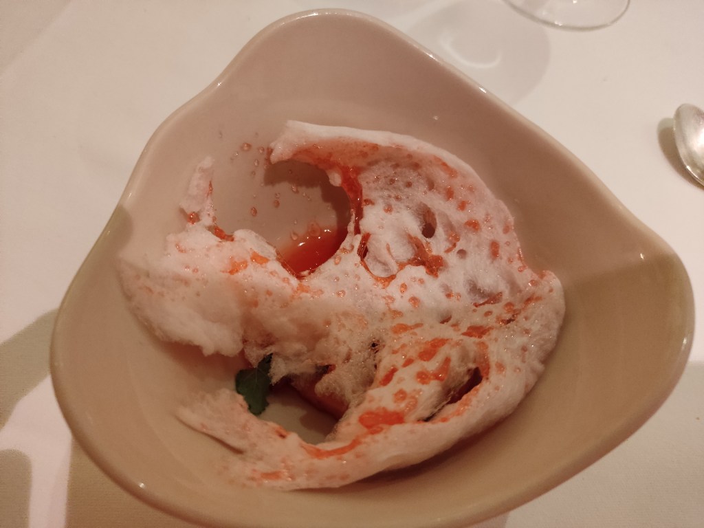 Candy floss which has been blow torched and is hard and streaked with red, hiding a pile of strawberries underneath