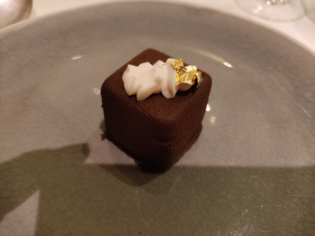 A chocolate covered cube, with a little bit of white crème fraiche on top and some gold leaf