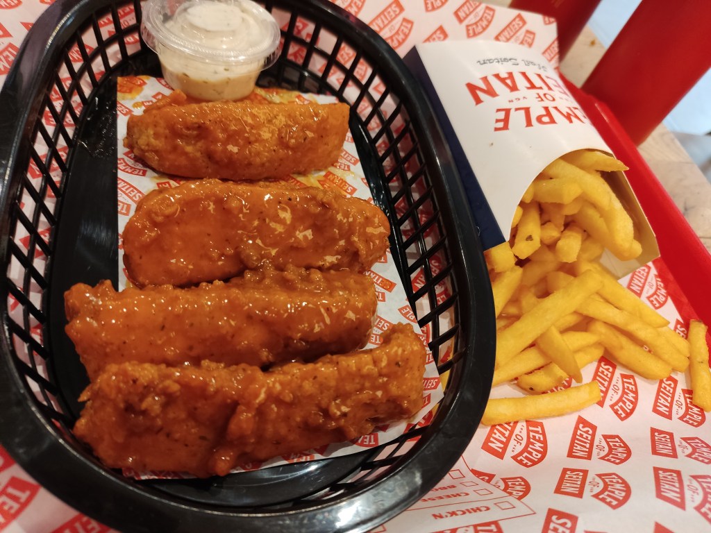 A tray with four sticky chicken wings and a pot of sauce and a carton of fries