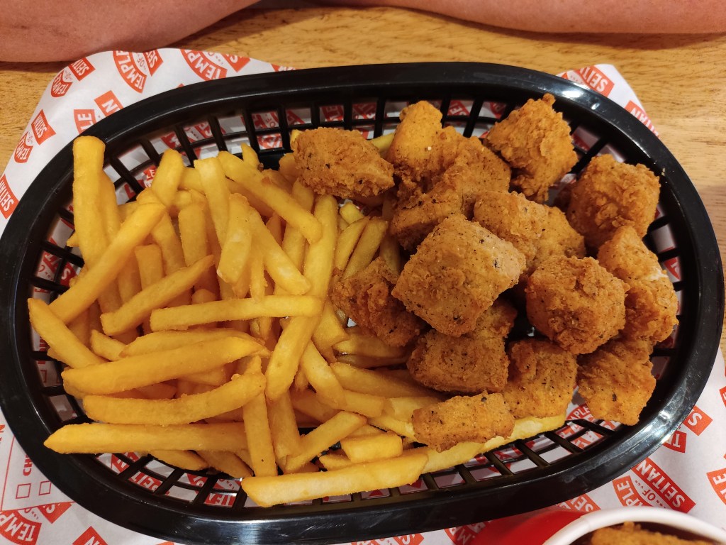 A tray with uniform chunks of battered popcorn chicken and a generous helping of fries
